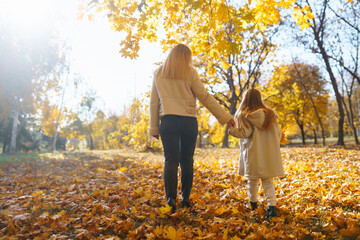 Beautiful Mom and daughter joyfully playing in vibrant autumn leaves at a sunny park on a clear day in October. Family day.