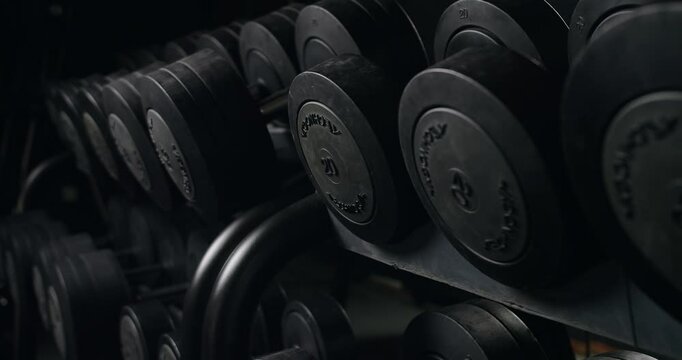 Close-up view of a row of black dumbbells neatly arranged on a rack in a dimly lit gym, focusing on fitness and strength training equipment. Row of Black Dumbbells in a Gym Setting, Exercise Equipment