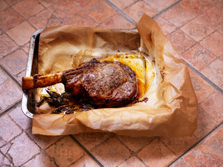 A piece of cooked meat on the bone is sitting on a cooking paper and tray with a few herbs on top....