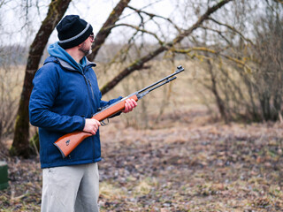 A man in a blue jacket is holding a shotgun. The image has a mood of excitement and anticipation,...