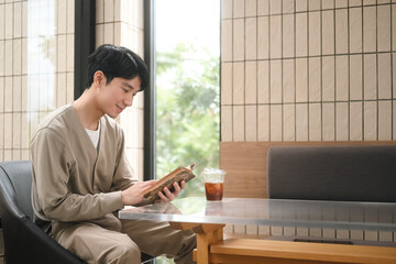 A man enjoys a quiet moment reading a book with a glass of iced coffee by his side, sitting in a serene and cozy cafe
