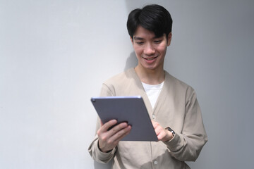 A young man is smiling as he looks at a tablet, He is wearing a tan sweater and he is enjoying his time with the device