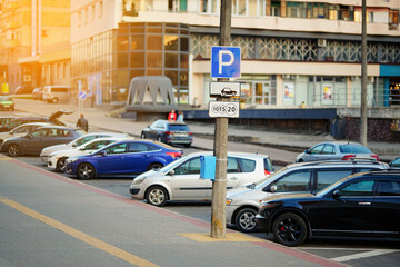 City parking lot with row of parked cars and paid parking sign on pole, parking problems and the role of paid parking zones in urban management.