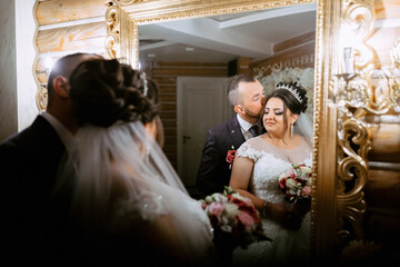 A bride and groom are kissing in front of a mirror