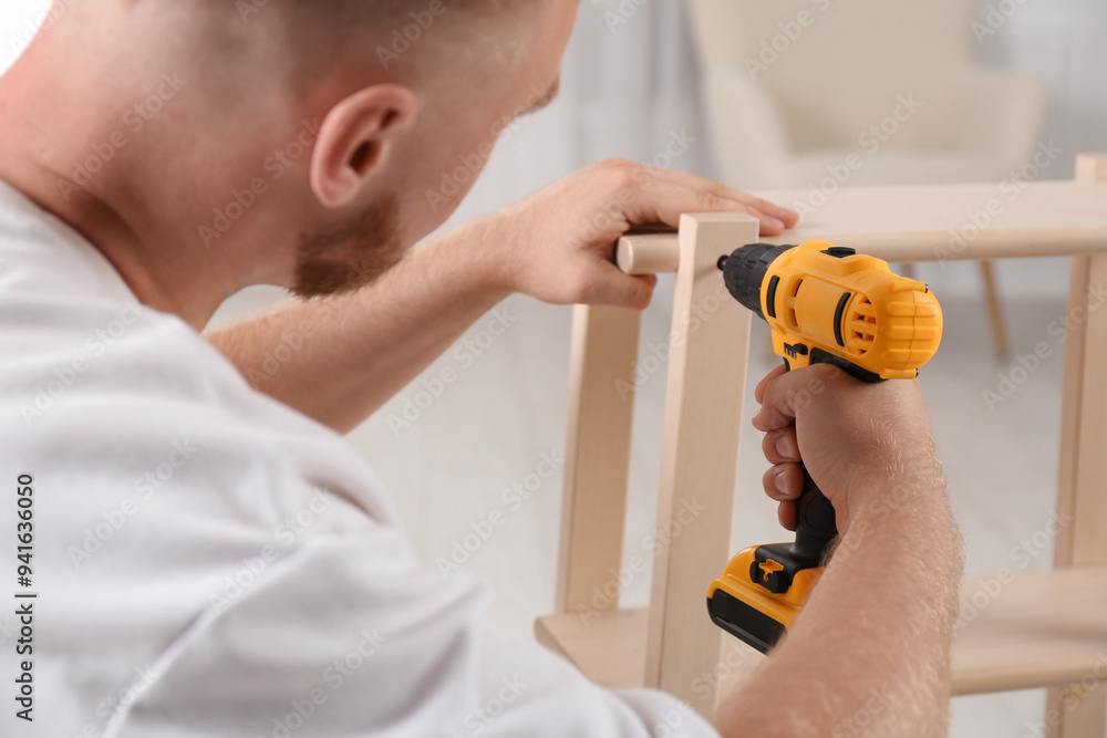 Sticker Man with electric screwdriver assembling furniture in room, closeup