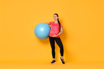 Beautiful pregnant woman with fitball on yellow background