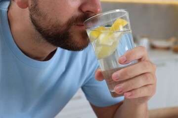 Fototapeta premium Man drinking water with lemon indoors, closeup