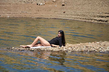 beautiful young brunette latin woman in black shirt and black bikini lying relaxed on the shore of...
