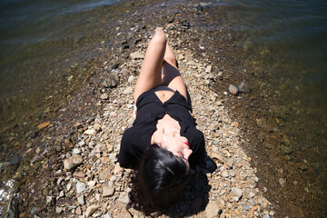 Pretty young brunette latin woman with red lips and dressed in black shirt and black bikini lying...