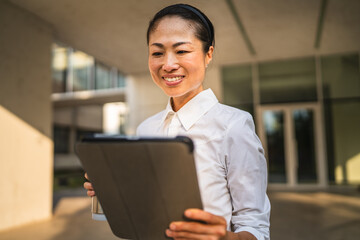 Mature japanese business woman use digital tablet and hold thermos
