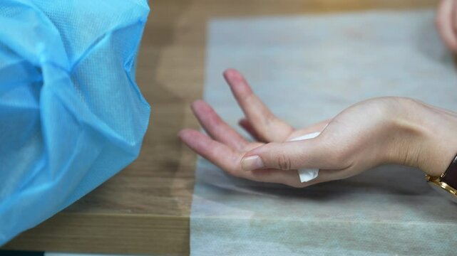 Female hand holding a little piece of napkin behind her thumb. Medic in latex gloves uses scarifier to take patient's blood test. Close up.