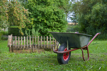 Wheelbarrow next to a fenced vegetable bed on the lawn in a natural garden, seasonal gardening for organic homegrown food in the backyard, copy space, selected focus