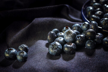 Ripe blueberries rolling on a dark purple napkin, dark and moody still life with fruits, copy space, selected focus