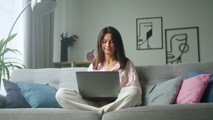 Young woman sitting on sofa using laptop at home