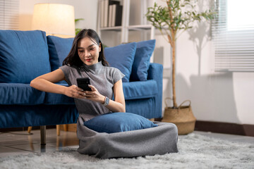 Obraz premium Young woman using smartphone at home on living room floor