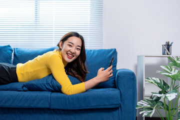 Obraz premium Happy young woman relaxing on couch using smartphone at home