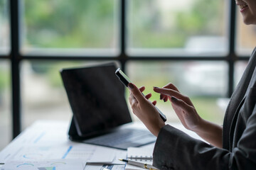 Businesswoman working using smartphone in office with charts and tablet on desk