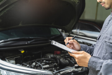 Auto check up and car service shop concept. Mechanic writing job checklist to clipboard to estimate...