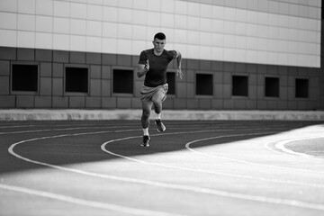 Black and white filter. Young athletic m,an, sprinter picks up speed before finish line to win. Dynamic photo. Concept of sport, tournament, motivation, workout, competition. Ad