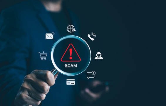 Scam Alert Warning with Cybersecurity Icons. A person holding magnifying glass highlighting warning sign for scams with icons representing online threats, phishing, and cybersecurity. Unknown person,