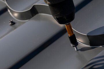 Close-up of power drill fastening screw to metal roofing sheet.