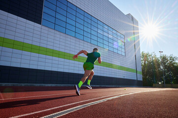 Obraz premium Focused and fast, athlete in green races along track, with the sleek building facade adding modern touch to his sprint. Concept of sport, tournament, motivation, workout, competition. Ad