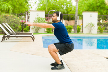 Full lenght view of a young athlete is doing squats by the pool in his backyard on a sunny summer...