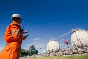 team of engineers in safety gear conducts an inspection of the construction and operation of the oil and gas plant behind the construction site. A handsome technician is working in high security area.