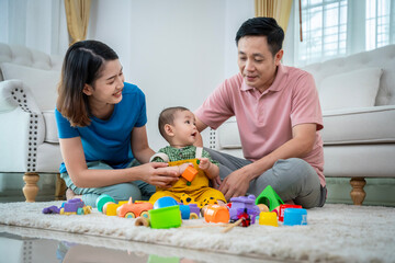 A family of three, a man and two women, are playing with toys on the floor. The baby is holding a toy truck and the parents are clapping. Scene is happy and playful