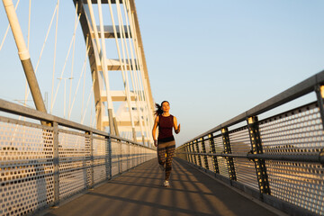 Woman enjoying her morning run on a sunny bridge surrounded by serene outdoor scenery and a clear...