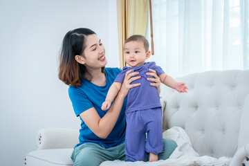 A woman is holding a baby in a blue outfit. The scene is happy and joyful