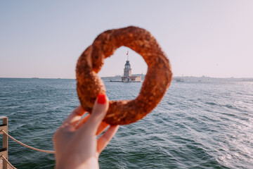 A girl enjoys a fresh simit bagel from a cafe in Istanbul, with the iconic Maiden's Tower and...