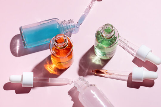 Colorful serum bottles with droppers on pink backdrop