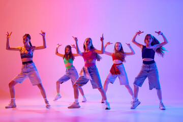 Group pf girls, dancers dancing dressed stylish sport, casual outfits in neon light against gradient pink background. Concept of sport and hobby, childhood, friendship, motion. Dance school.