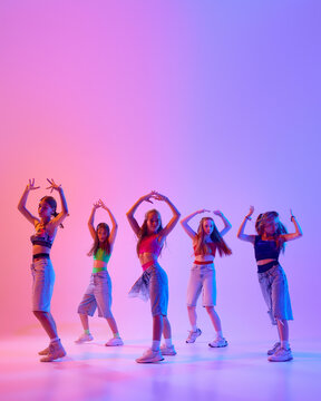Poster. Group of artistic young girls dressed casual, sport attire moves in synch in neon light against gradient pink background. Concept of sport and hobby, childhood, motion. Dance school.