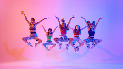 Energetic photo of artistic and sporty teenage girls performing in neon light against gradient pink background. Concept of sport and hobby, childhood, friendship, motion. Dance school.