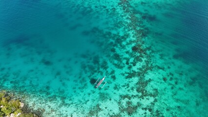 Traditional indonesian boat floating on the ocean above a reef atoll with clear blue water ready for diving and snorkeling. Bird view. Togean National Park, Sulawesi, Indonesia.
