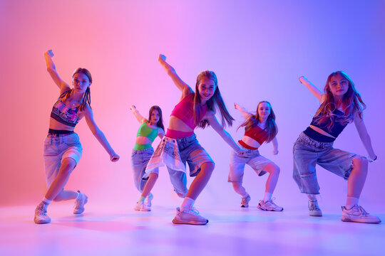 Performance radiates energy as dancers, girls move in perfect harmony in neon light against gradient pink background. Concept of sport and hobby, childhood, friendship, motion. Dance school.