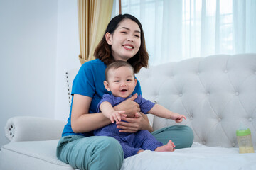 A woman is holding a baby on a couch. The baby is smiling and the woman is smiling back. Scene is happy and loving 