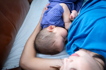 A woman is laying on a couch with a baby on her chest. The baby is sleeping and the woman is...