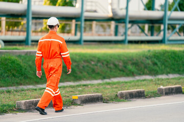 An engineer in an orange jumpsuit walks through an industrial plant inspecting pipelines. worker and factory are reflects the importance of safety and thorough inspections in industrial operations.