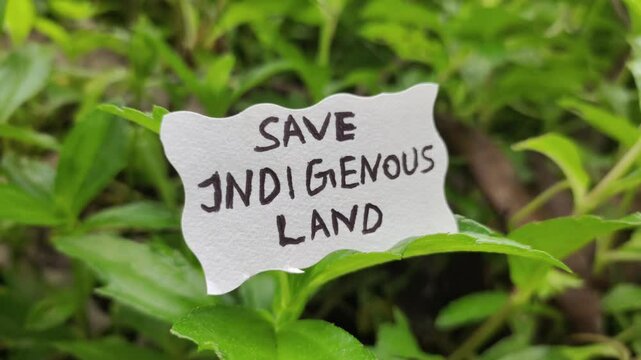 Save Indigenous land word letters text handwritten calligraphy design on white paper label note isolated on a natural green leaves nature background. Closeup macro side view.