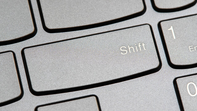 Man pressing the shift key on a modern laptop computer keyboard closeup top view, one person. Shift button key, shifting changing simple abstract concept, capital letters, special characters symbol