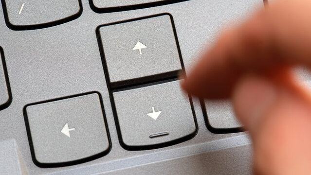 Man pressing the up arrow key on a modern laptop computer keyboard, closeup detail, slow motion. Moving forward in corporate business, way ahead, front, going towards end goals symbol abstract concept