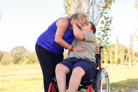 Young man in wheelchair giving affection to woman outdoors