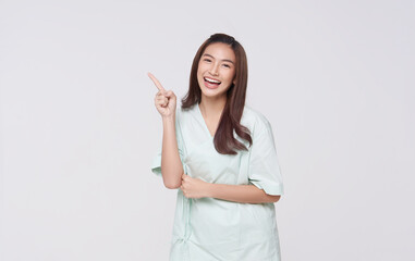 Young Asian woman wearing patient outfits pointing finger presenting to copy space for product isolated on white background. advertisement life insurance