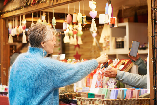 Outdoor portrait of beautiful middle age woman with grey hair buying gifts and souvenirs at Christmas market