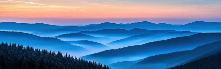 Obraz premium Misty blue mountains at dawn with soft light over forested hills