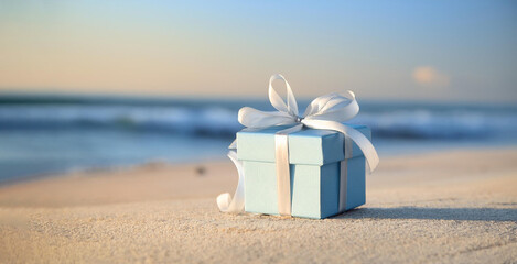 Naklejka premium A small, pastel blue gift box with a white ribbon is placed on a sandy beach