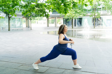 Woman and sports, exercise for weight loss in the fresh air. Happy curvy 40s woman doing workout routine outdoor at city park